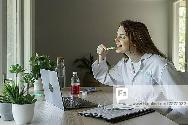 Junge Zahnärztin unterrichtet Zähneputzen per Videoanruf auf dem Laptop zu Hause