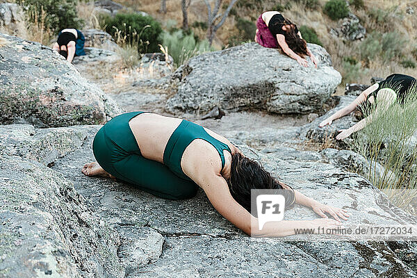 Flexible female friends practicing yoga on rocks