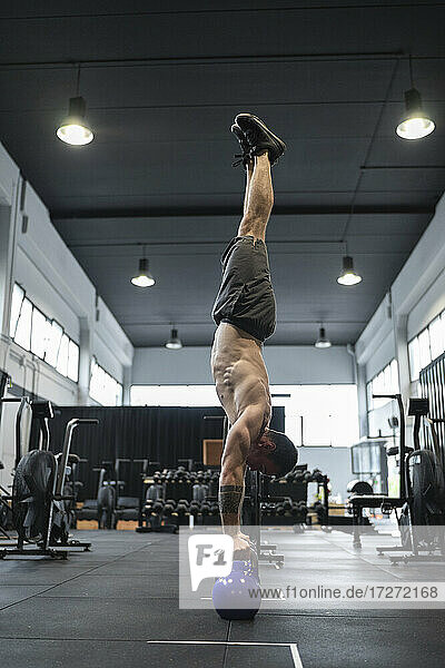 Male athlete balancing upside down on kettlebells in gym