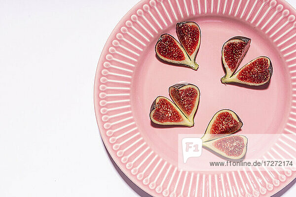 Directly above shot of fig slices arranged in pink plate over white background
