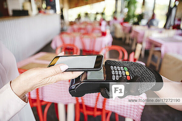 Reife Frau  die ihre Rechnung mit dem Handy bezahlt  während sie im Restaurant steht