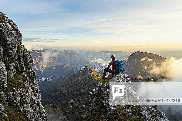 Nachdenklicher Wanderer  der die Aussicht betrachtet  während er bei Sonnenaufgang auf einem Berggipfel in den Bergamasker Alpen  Italien  sitzt