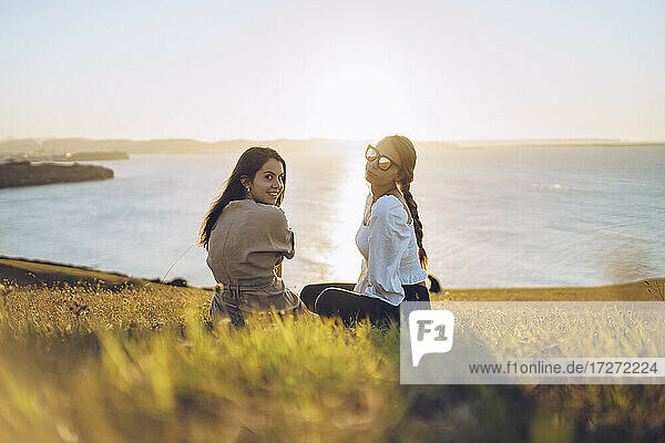Young female friends sitting on hill at Mirador de La Providencia  Gijon  Spain