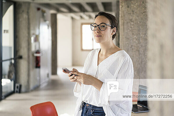 Geschäftsfrau schaut weg  während sie im Büro ein Mobiltelefon benutzt