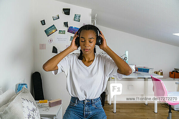 Betrachtendes Teenager-Mädchen  das über Kopfhörer Musik hört  während es im Schlafzimmer zu Hause sitzt