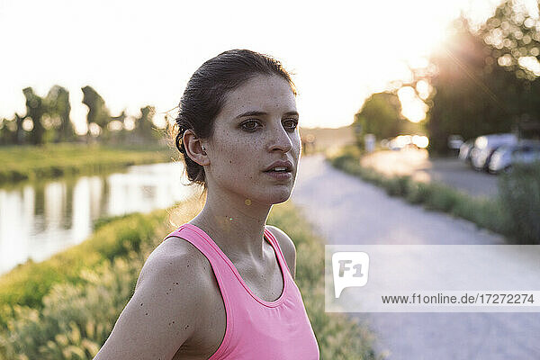 Confident sportswoman looking away while standing in park during sunset