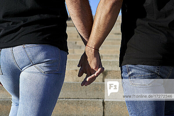 Schwules Paar hält sich an den Händen  während es auf einer Treppe steht