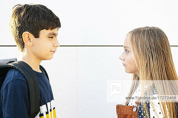 Ernster Bruder und ernste Schwester schauen sich an  während sie an einer Mauer an einem sonnigen Tag stehen