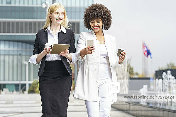 Geschäftsfrauen  die ein digitales Tablet und ein Smartphone benutzen  während sie vor einem Gebäude stehen