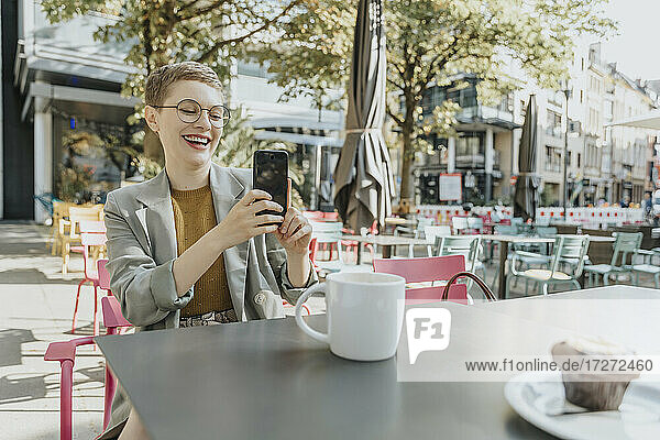 Frau  die ein Selfie mit ihrem Smartphone macht  während sie in einem Café im Freien sitzt