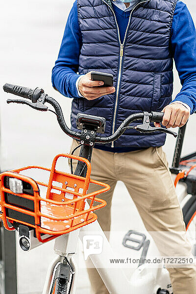 Junger Mann benutzt sein Smartphone  während er mit dem Fahrrad steht