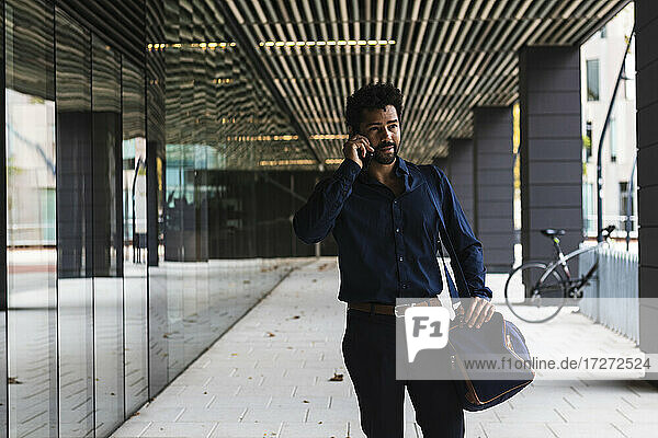Contemplating entrepreneur with bag talking on smart phone in city