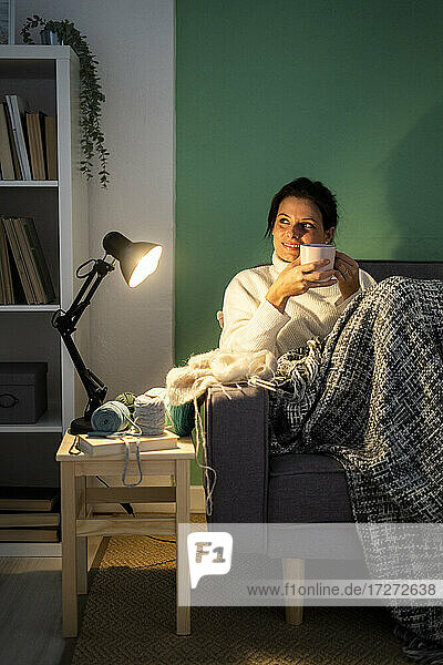 Mittlere erwachsene Frau hält Kaffeetasse  während sie zu Hause auf dem Sofa sitzt