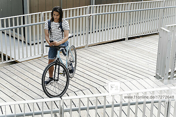 Blick von oben auf einen Mann mit einer Beinprothese  der ein Mobiltelefon auf einem Fahrrad in der Stadt benutzt