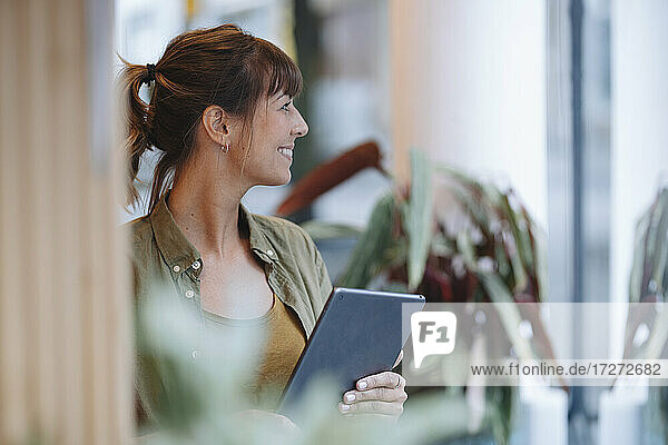 Weibliche Unternehmerin schaut weg  während sie ein digitales Tablet in einem Café hält