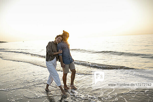 Junges Paar  das bei Sonnenuntergang am Strand spazieren geht