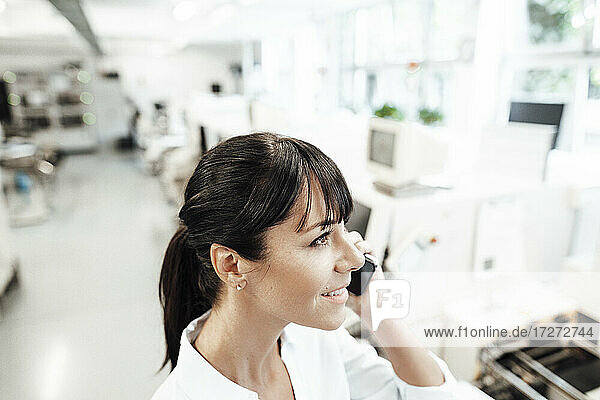 Smiling businesswoman talking on smart phone while looking away in industry