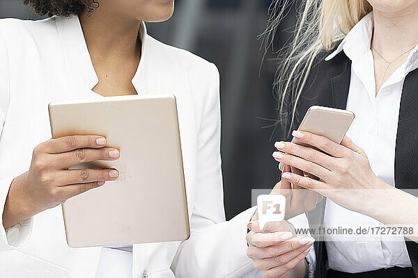 Geschäftsfrauen tauschen Mobiltelefon und digitales Tablet mit einem Kollegen im Freien aus