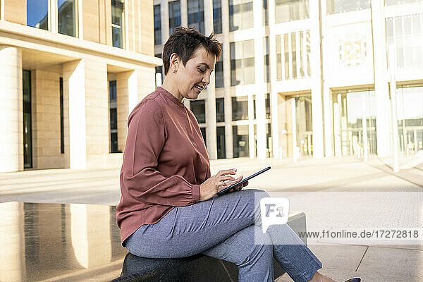 Businesswoman using digital tablet while sitting on bench in city