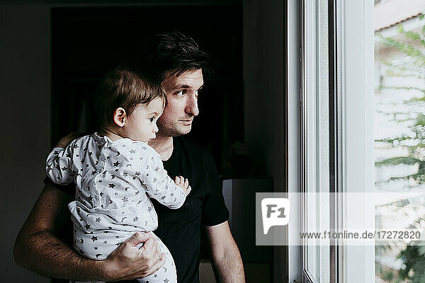 Father carrying son while standing looking through window at home