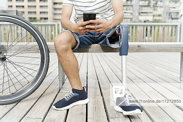 Tiefschnitt eines Mannes mit Beinprothese  der in der Stadt ein Mobiltelefon benutzt