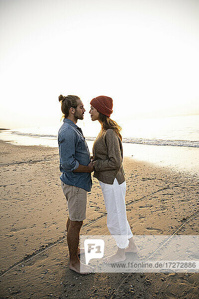 Romantisches junges Paar  das sich bei Sonnenuntergang am Ufer stehend anschaut und die Hände hält