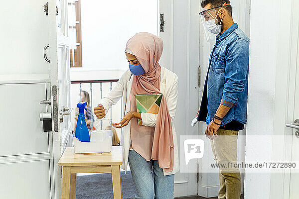 Frau mit Gesichtsmaske wäscht sich die Hände  während sie neben einem Mitarbeiter am Büroeingang steht