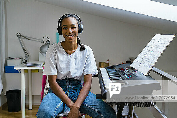 Smiling teenage girl with wearing headphone sitting on chair at home