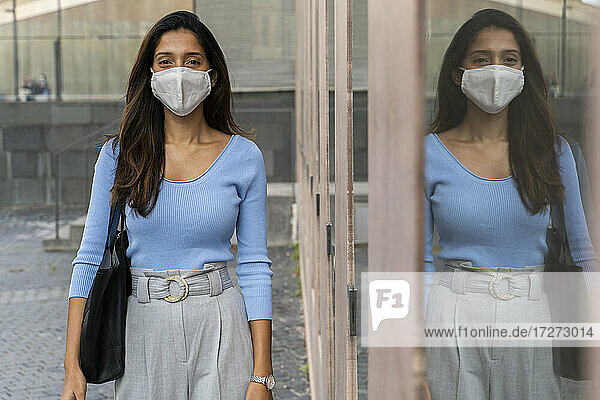 Junge Geschäftsfrau mit Schutzmaske an einem Glasfenster während der Pandemie