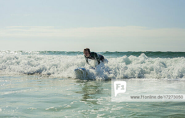 Teenage boy surfing in sea against sky at beach