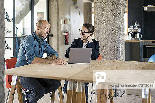 Man and woman using laptop while sitting by table at office