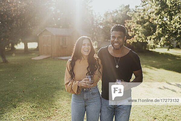 Smiling couple drinking wineglass while standing at backyard