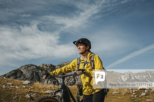 Lächelnde Frau  die mit einem elektrischen Mountainbike gegen einen Berg im Naturpark Somiedo  Spanien  fährt