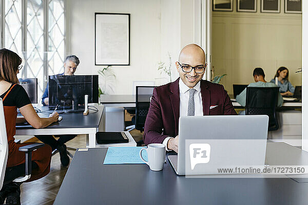 Smiling bald businessman working on laptop at desk in office