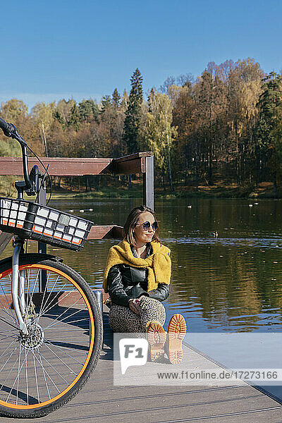 Lächelnde Frau entspannt sich mit dem Fahrrad auf dem Steg über dem See an einem sonnigen Tag