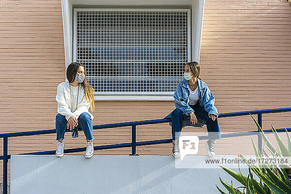 Freundinnen schauen sich an  während sie auf einem Geländer sitzen