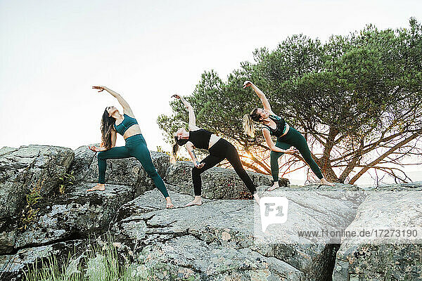Freundinnen üben Yoga auf Felsen gegen den klaren Himmel am Wochenende