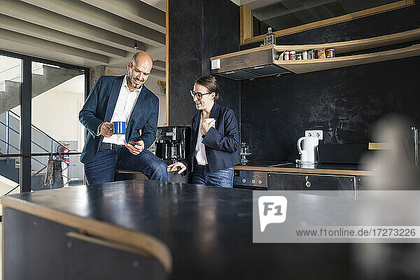 Geschäftsleute  die ein Mobiltelefon benutzen  während sie im Büro Kaffee trinken