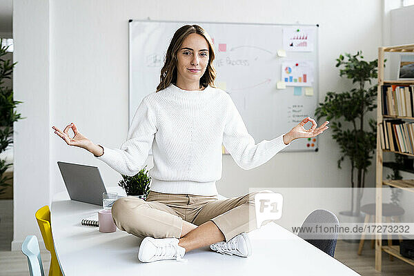 Junge Geschäftsfrau macht Yoga  während sie auf dem Tisch im Büro sitzt