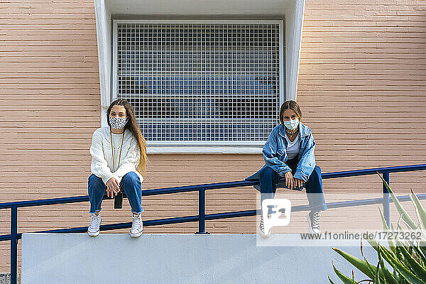 Teenager-Freunde distanzieren sich  während sie mit Gesichtsschutzmaske auf dem Geländer sitzen  während covid-19