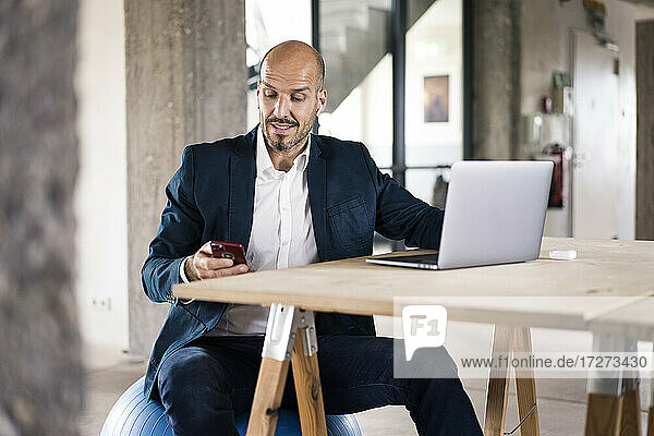 Man wearing suit using laptop and mobile phone while sitting at office