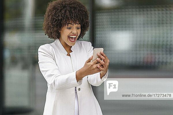 Glückliche Geschäftsfrau  die im Freien stehend auf ihr Mobiltelefon schaut
