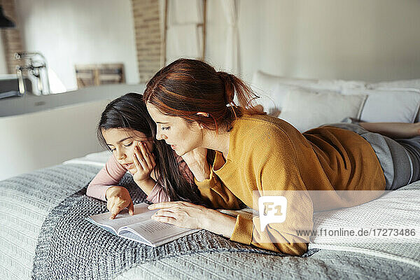 Mother and daughter reading book while lying on bed at home