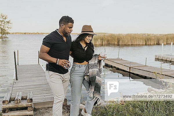 Mann und Frau mit Weinglas in der Hand beim Spaziergang an der Seebrücke