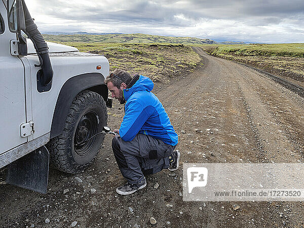 Man kneeling while examining tire pressure through equipment at roadside