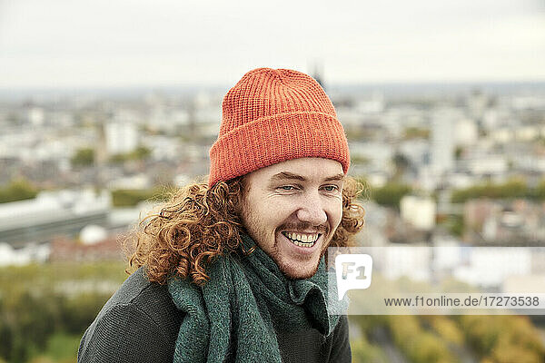 Cheerful redhead man wearing knit hat against city
