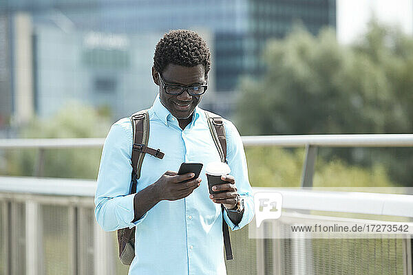 Lächelnder Mann mit Textnachrichten auf einem Smartphone in der Stadt stehend