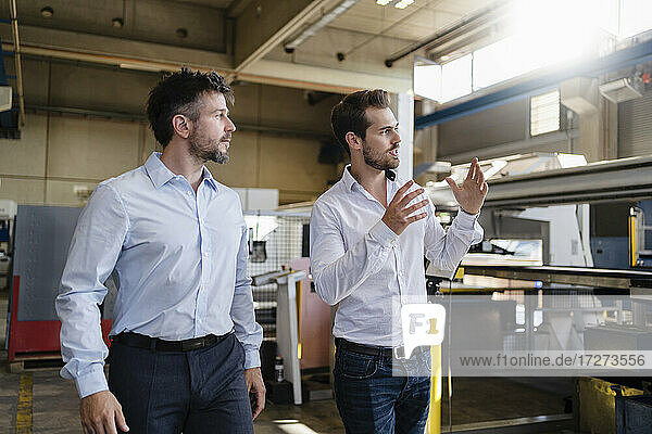 Young businessman looking away while having discussion with colleague at modern factory