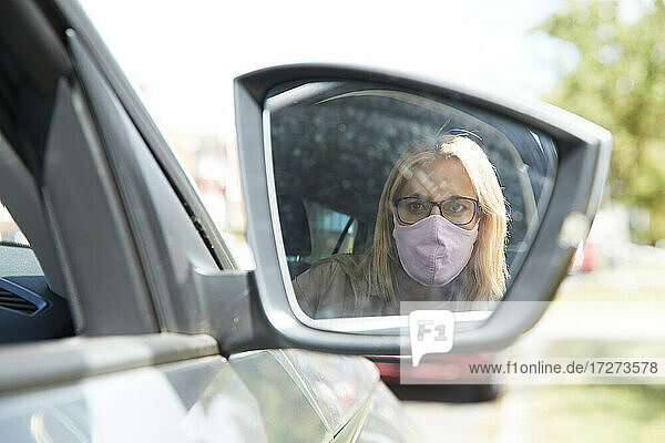 Spiegelung einer Frau mit Gesichtsschutzmaske  die im Auto sitzt