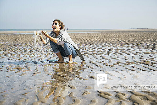 Fröhliche junge Frau spielt mit Wasser am Meer